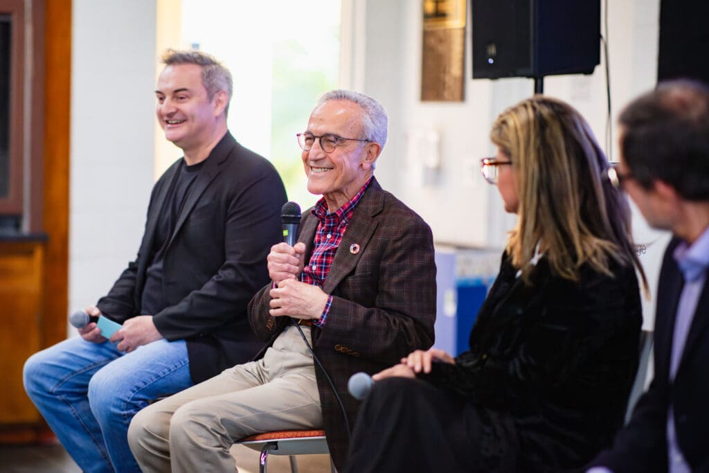 Four panelists sit side-by-side during the event. The center speaker, smiling warmly, looks engaged as the three speakers on either side listen attentively.