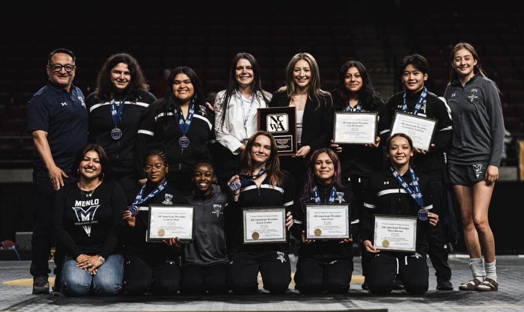 A women's sports team, smiling and posing with medals and certificates on a stage. They wear matching tracksuits, exuding pride and accomplishment.