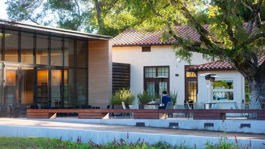 Buildings in the daylight surrounded by trees and outdoor seating.