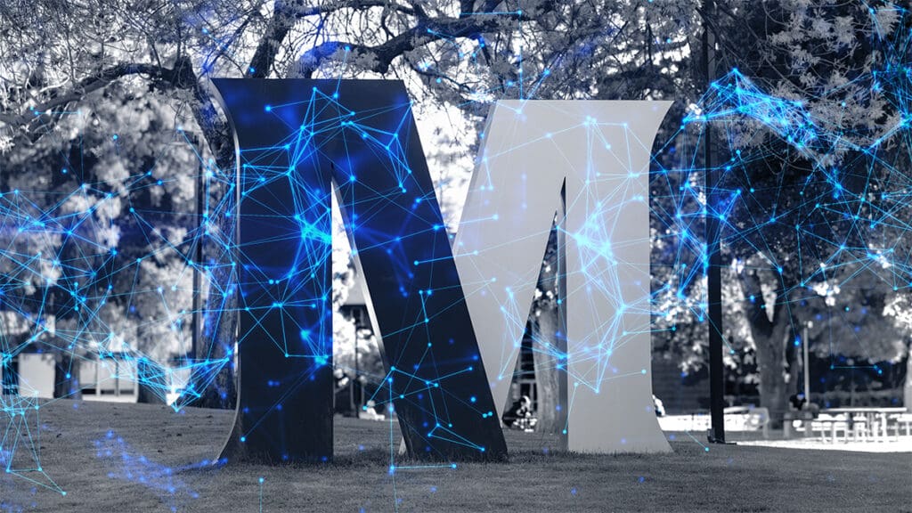 A large black and white letter "M" sculpture stands on grass with trees in the background, overlaid with futuristic blue digital network patterns.
