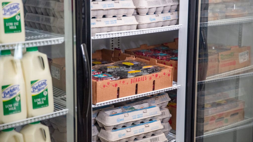 Grocery store cooler with cartons of low-fat milk, stacks of egg cartons, and boxes of fresh berries, conveying a fresh and organized atmosphere.