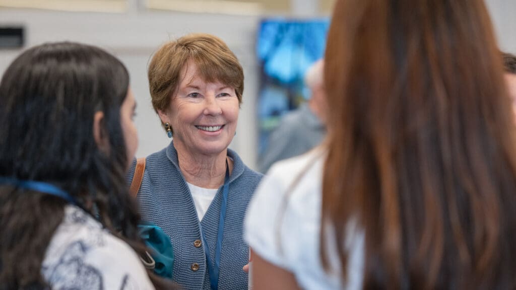 A woman in professional attire speaks with two students with a warm smile.