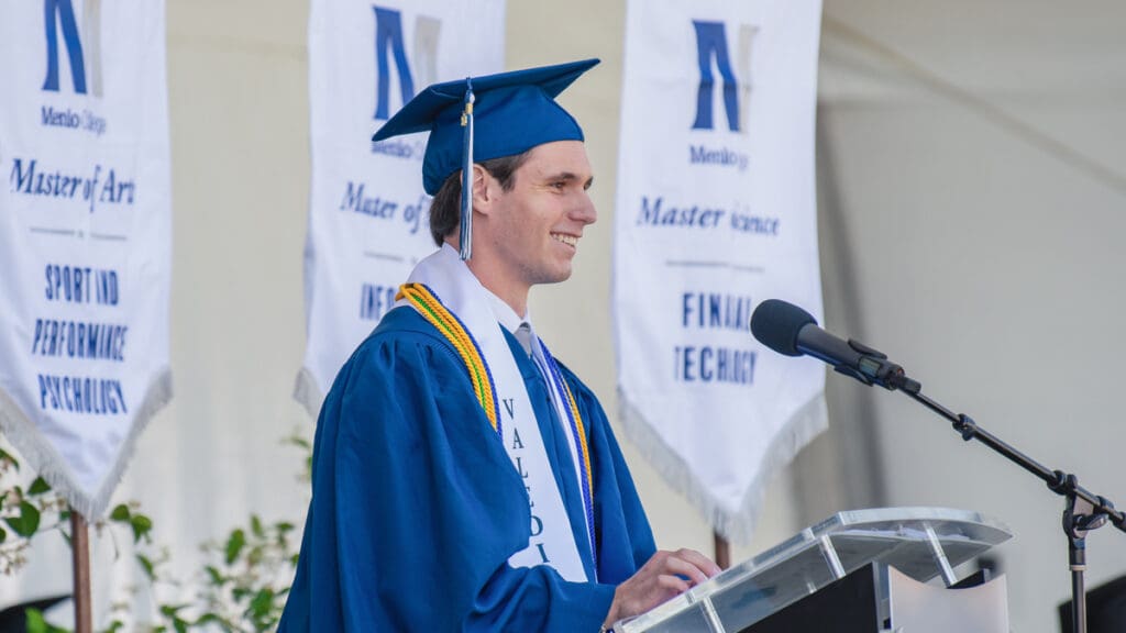 A student in graduation attire delivers a speech.