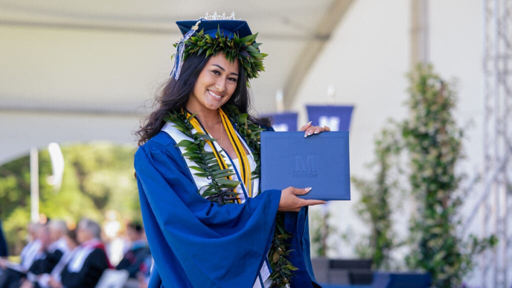 A student at graduation is holding up her diploma.