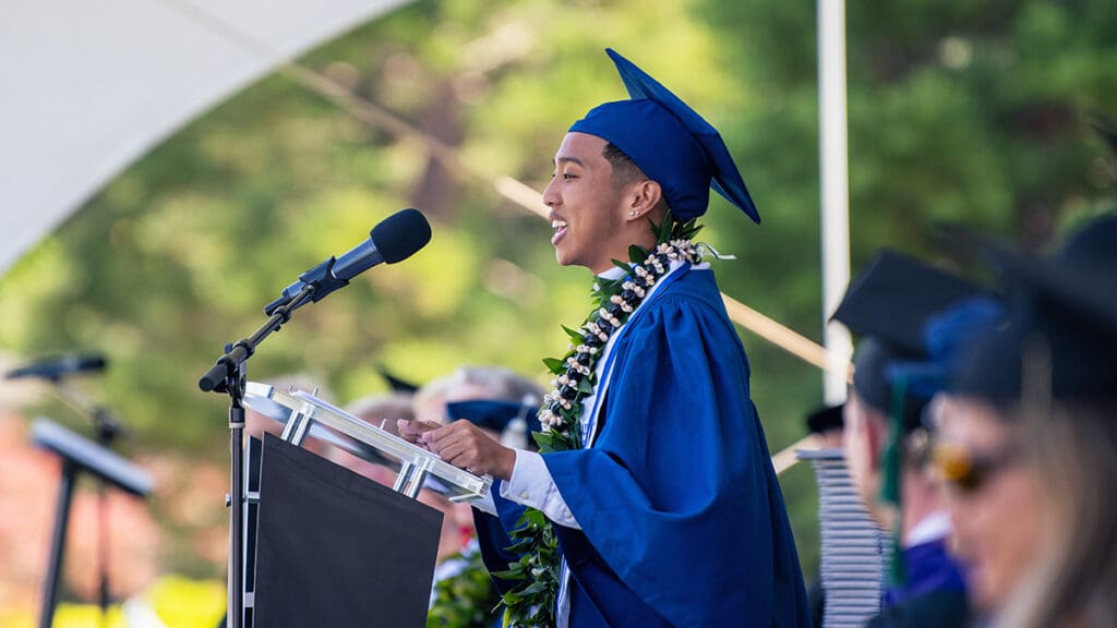 A student in graduation attire delivers a speech.