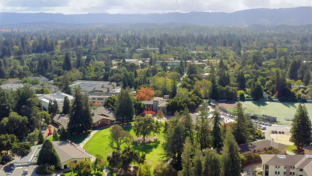 Aerial view of Menlo College’s campus in Atherton, California, surrounded by trees and residential neighborhoods, with academic buildings, athletic facilities, and the Silicon Valley landscape visible in the distance.
