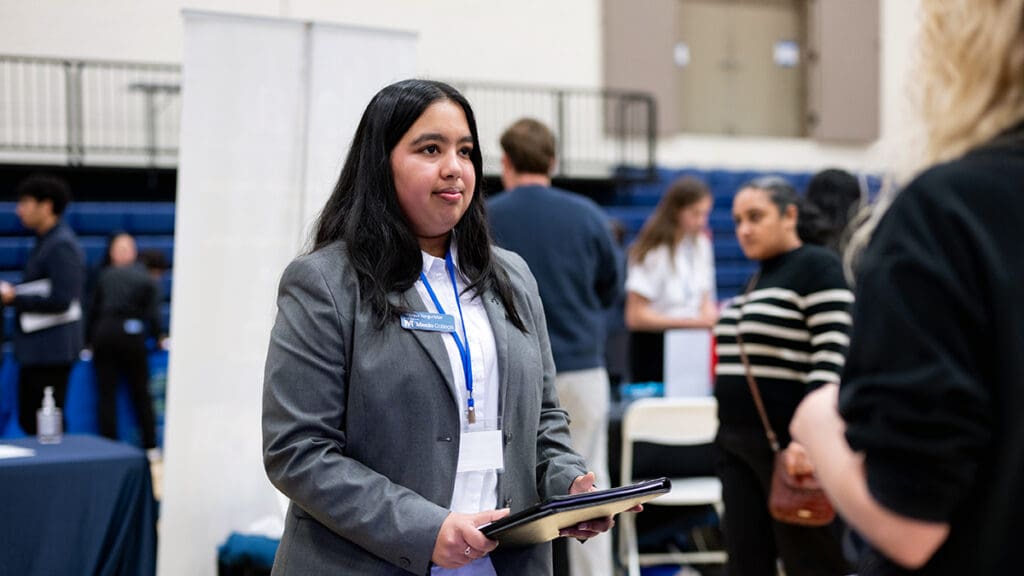 Menlo College student Ananyaa Vengurlekar speaks with an employer while holding a portfolio at Career Connect Day 2026 on the Menlo College campus.