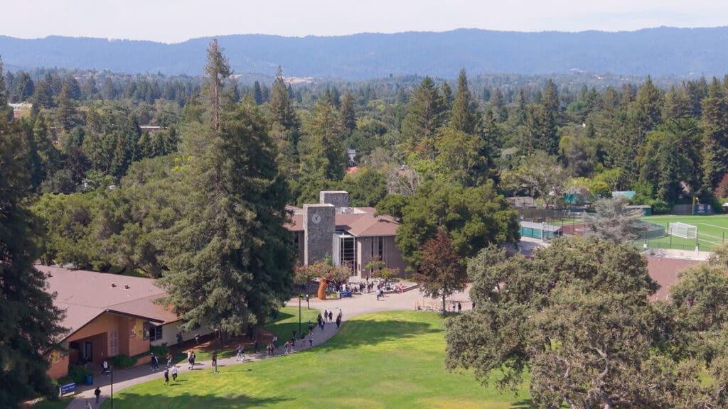 Aerial view of Menlo College’s Atherton campus showing students walking across the quad, campus buildings, athletic fields, and surrounding trees.