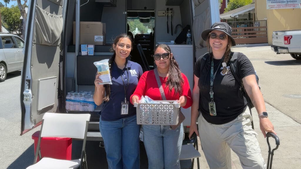 Menlo College student Martha Zurita-Ortez stands with two fellow volunteers beside a community outreach van during her summer internship with the Santa Cruz County Safe Drug Use and Overdose Prevention Program.