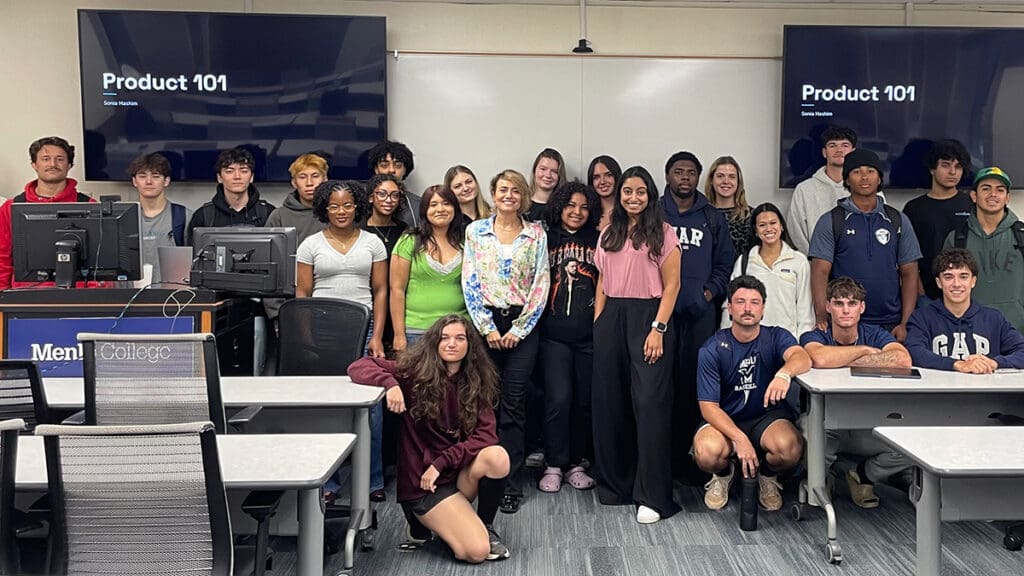 Dr. Marzieh Yaghini stands at the center of a group of Menlo College students posing for a photo in a classroom following a guest presentation on product development and marketing.