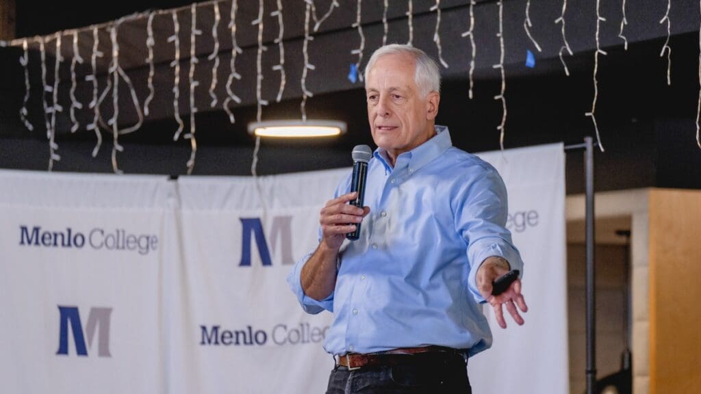 Bill Reichert, General Partner at Pegasus Tech Ventures, speaks into a microphone and gestures toward the audience while delivering a keynote at Menlo College’s Finance Hybrid Conference 2026.