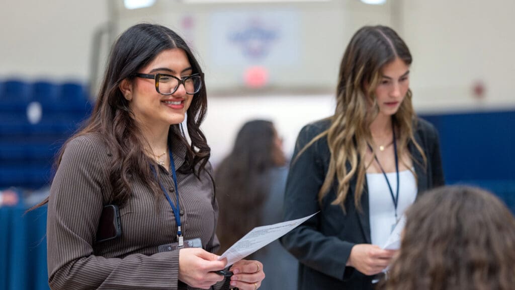 Two Menlo College students wearing professional attire and name badges hold informational materials while participating in Career Connect Day.