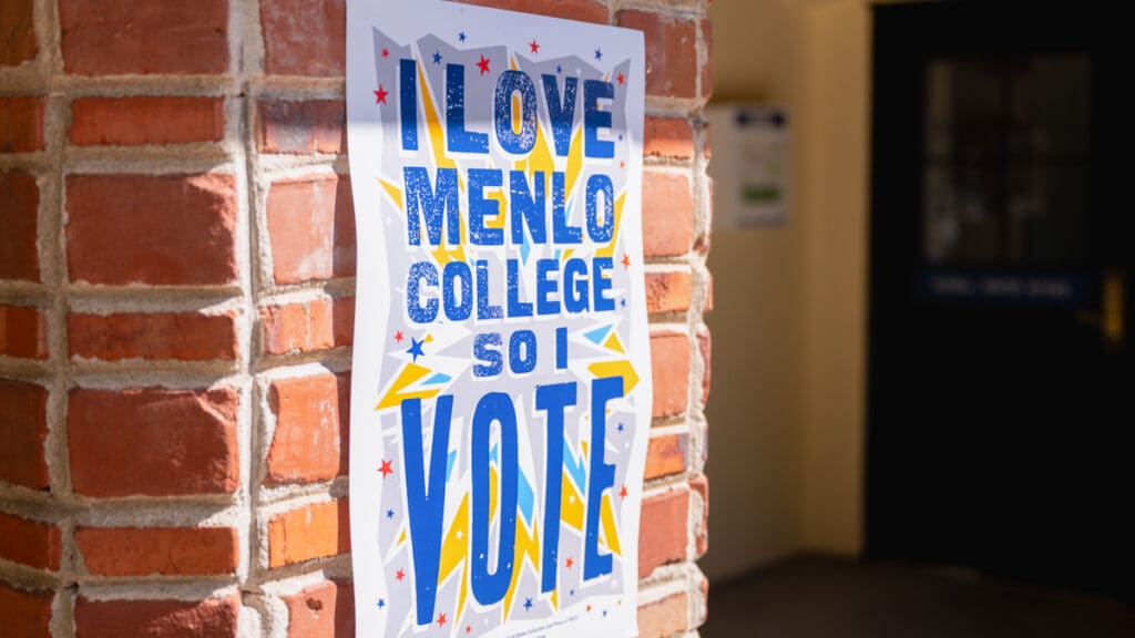 A colorful “I Love Menlo College So I Vote” poster hangs on a brick pillar at the entrance to Menlo College’s Russell Center, promoting student civic engagement and voter participation.
